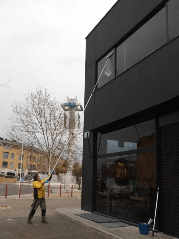 Profesional de empresa de limpieza en Pozuelo limpiando ventanas altas de un local comercial con pértiga extensible