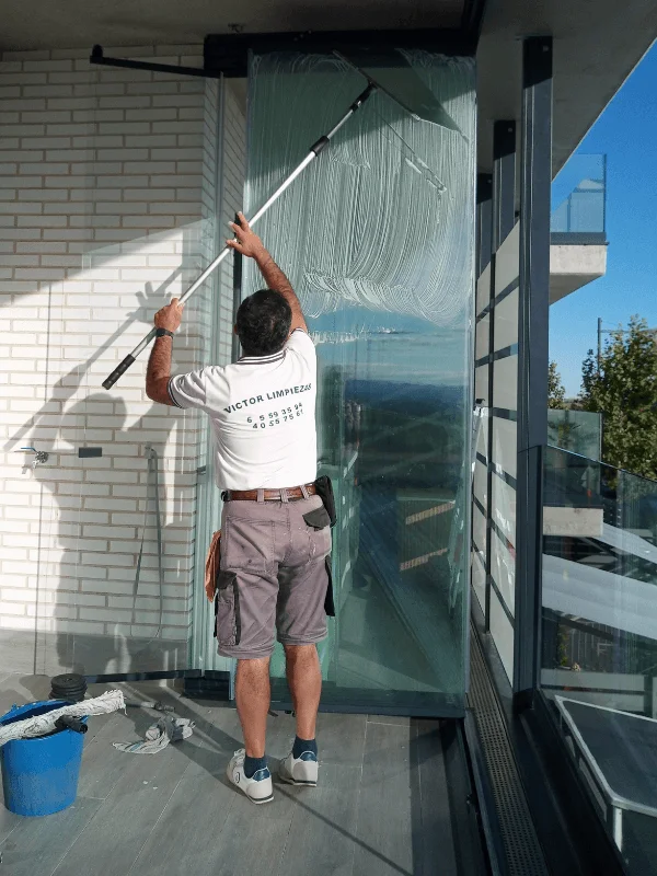 Empleado de empresa de limpieza en Las Rozas limpiando cristales exteriores en una terraza acristalada con herramienta profesional